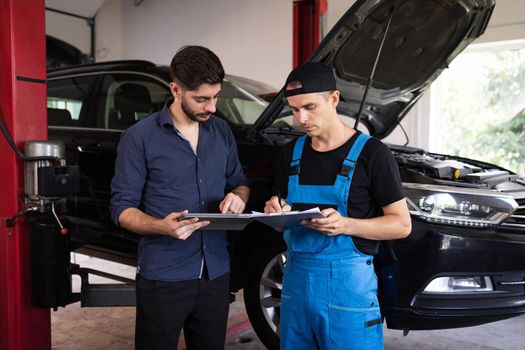 Manager Checks Data on a Tablet Computer and Explains the Breakdown to Mechanic. Car Service Employees Inspect the Bottom and Skid Plates of the Car. Specialist is Showing Info on Tablet