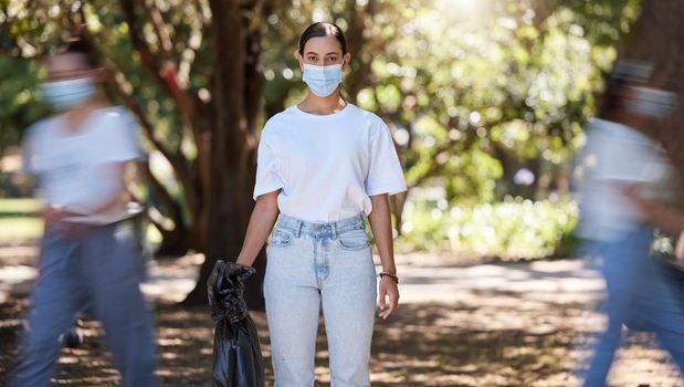 Female wearing covid mask cleaning the park for a clean, hygiene and safe green outdoor environment. Community service, volunteers or activist workers with rubbish, trash and garbage in a plastic bag.
