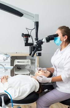 Female dentist using dental microscope treating patient teeth at dental clinic office. Medicine, dentistry and health care concept