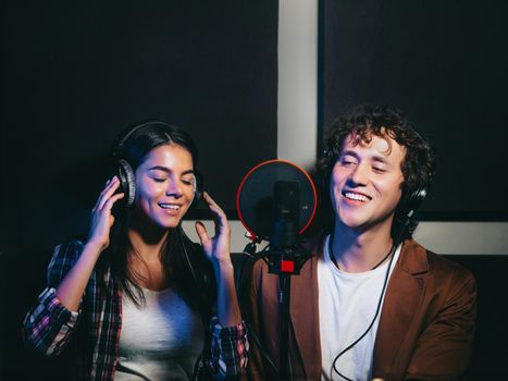 Two young singers performing their song in record studio. Professional musician duet recording new album CD. Beautiful couple working together. High quality photo
