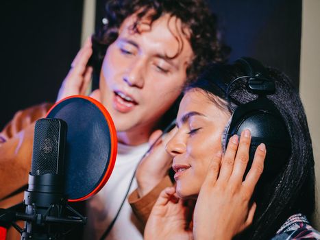 Two young singers performing their song in record studio. Professional musician duet recording new album CD. Beautiful couple working together. High quality photo