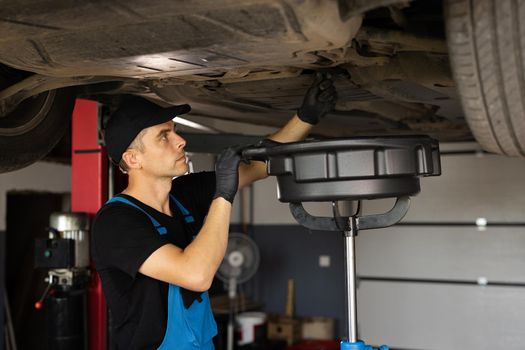 Changing the oil in a car engine. Car engine oil replacement. Car maintenance, car mechanic replaces the oil in the engine. Mechanic drain the old oil from the engine through the drain plug.