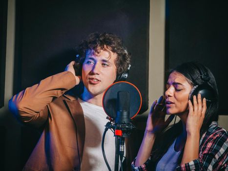 Two young singers performing their song in record studio. Professional musician duet recording new album CD. Beautiful couple working together. High quality photo