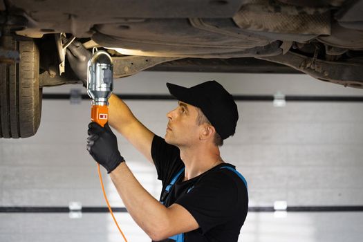 Male car mechanic checking car. Auto mechanic working underneath car lifting machine at the garage. Working in car repair shop and running small feminine business concept.