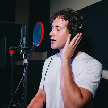 Male vocal artist with curly hair singing alone. Young handsome singer man emotionally writing song in the studio. Recording new melody or album. High quality photo