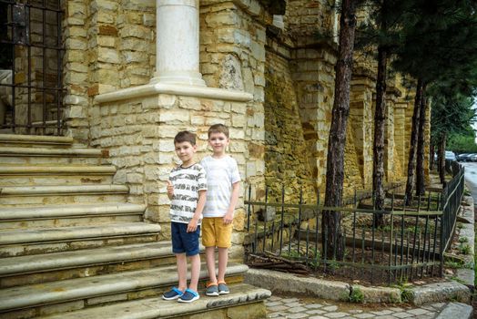 Two little boys with modern haircuts near the stairs in colorful T-shirts and single tone pants. Concept of modern little boys.