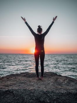 Slim woman in black bodysuit practicing yoga near sea or ocean during sunrise light. Flexibility, stretching, fitness, healthy lifestyle. High quality photo