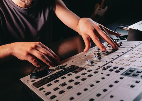 Unrecognizable sound producer or engineer rotates scrolls wheel on mixing console in professional recording studio. Musician working on new song. Hands close up. High quality photo