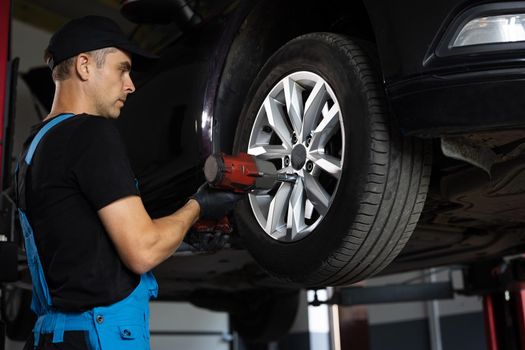 Car mechanic replacing car wheel of lifted automobile at repair service station. Assembly or dismantling of the wheels in the workshop. repair and maintenance of the car in service.