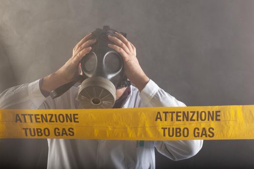 A medical engineer wearing an antigas mask during the gas leaks crisis and the emergency during the chaos. On the yellow tape the written notice "attention gas tube"