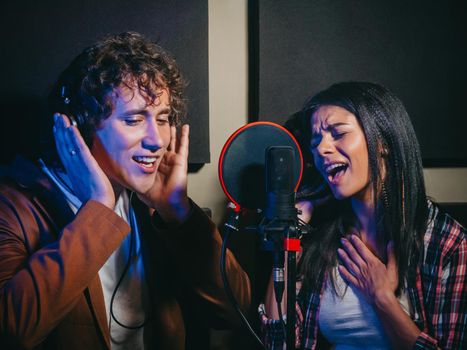 Two young singers performing their song in record studio. Professional musician duet recording new album CD. Beautiful couple working together. High quality photo