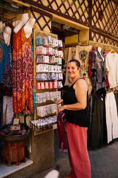 Happy female tourist smiling and looking at camera while choosing accessories on rack on clothes market
