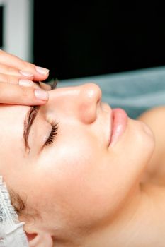 Side view fingers of female therapist making anti-age massage of forehead wrinkles to young caucasian woman in spa beauty salon