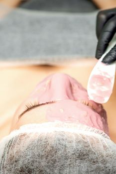 The cosmetologist applying an alginic mask to the face of a young woman in a beauty salon