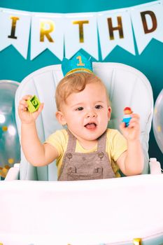 Cute baby boy sitting in his chair and playing with colorful bricks. Birthday handsome toddler child with big eyes portrait. Funny kid
