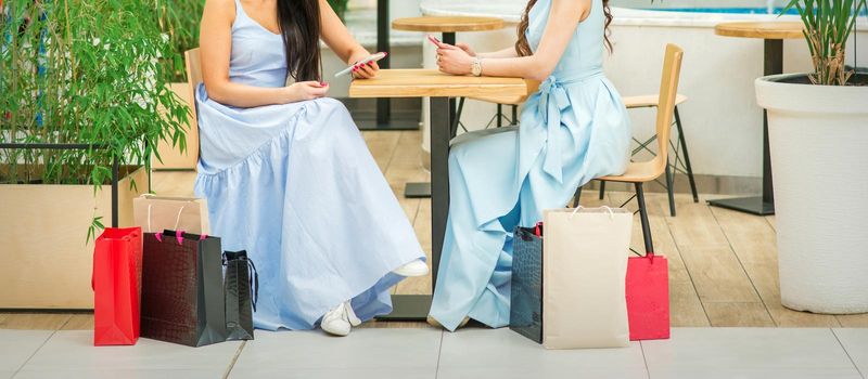 Two young women sitting at the table with smartphones and shopping bags in a cafe outdoors