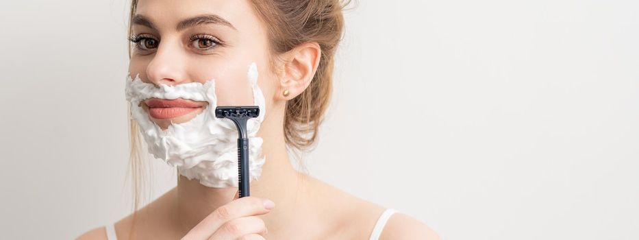 Beautiful young caucasian smiling woman shaving her face with razor on white background