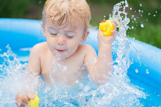 Cute little child bathing in blue street pool in courtyard. Portrait of joyful toddler, baby. Kid laughs, splashes water, smiles. Concept of healthy lifestyle, family, leisure in summer. quality photo