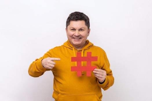Hashtag and blogging. Portrait of optimistic positive man pointing big paper hash symbol and smiling at camera, wearing urban style hoodie. Indoor studio shot isolated on white background.