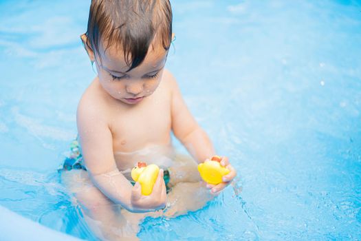 Cute little child bathing in blue street pool in courtyard. Portrait of joyful toddler, baby. Kid laughs, splashes water, smiles. Concept of healthy lifestyle, family, leisure in summer. quality photo