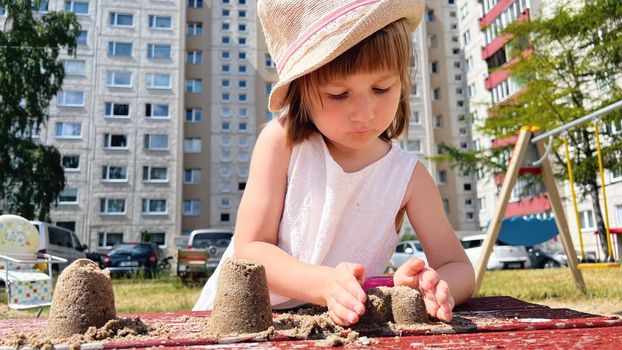SMALL GIRL IN SUMMER DRESS playing with sand in the backyard of urban block houses in Tallinn, Estonia