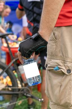 A plastic bottle of drinking water with a clean label in the hand of a cyclist athlete.