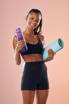 Fit body, healthy and athletic woman in studio holding mat and water bottle for yoga, pilates or exercise on pink background. Portrait of sporty, active or slim athlete ready for workout or training.