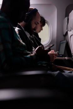 Multiethnic passengers flying in economy class with airplane, travelling on business work trip or holiday destination. Using laptop and phone on plane flight, international airways.