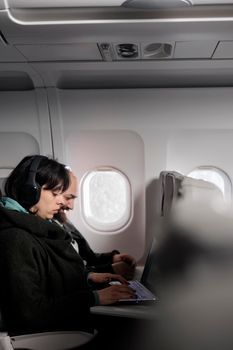 Tourists couple working on laptop and using mobile phone during commercial flight on airplane. People travelling to holiday destination with international airline, flying abroad.