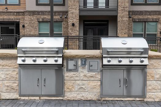 Two outdoor built in barbecue BBQ stainless steel grills at back yard of the residential complex with brick building on background