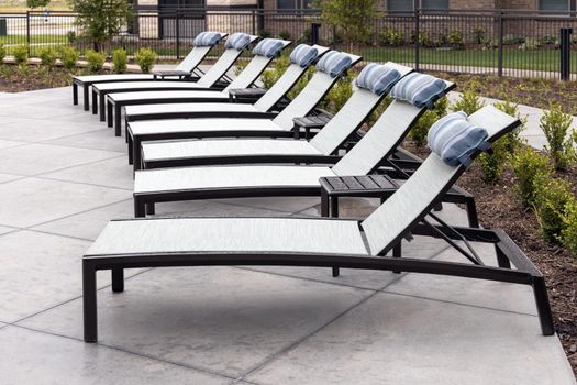 Empty sun loungers in the backyard of the residential complex, recreation area, many deck chairs with building on background