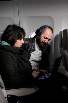 Couple travelling on holiday trip with aerial transportation, using laptop with online internet on commercial flight. Man and woman browsing computer on holiday destination, flying with plane.