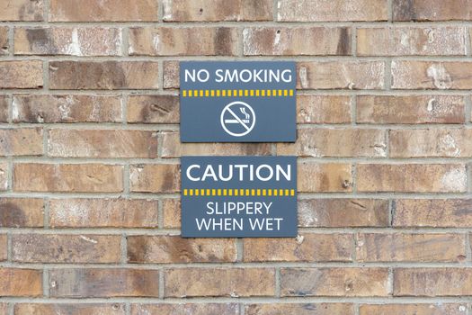Warning signs No smoking and Slippery when wet on brick wall, warning labels on gray plates