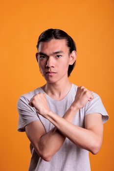 Confident young asian man showing stop gesture portrait, rejection, defense, decline concept. Teenager with crossed arms, clenched fists, confident facial expression looking at camera