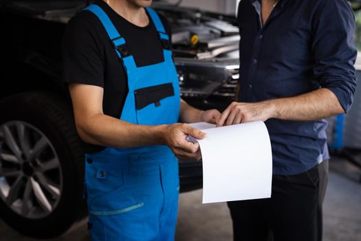 Mechanic and car owner signing paper at workshop. Customer and mechanic discuss upcoming car repair. Auto service, repair, deal and people concept.