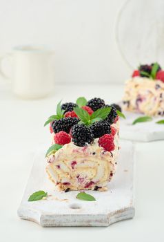 Baked meringue roll with cream and fresh fruits on a white wooden board, delicious dessert