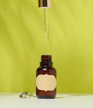 Brown glass bottle with a cosmetic product and a pipette, green background. Container for oils, gel, acids