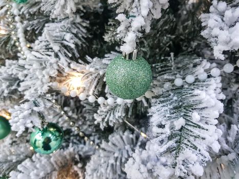 Green shiny balls on the Christmas tree. White pearl beads on spruce branches. The branches are covered with frost. Christmas or New Year background.