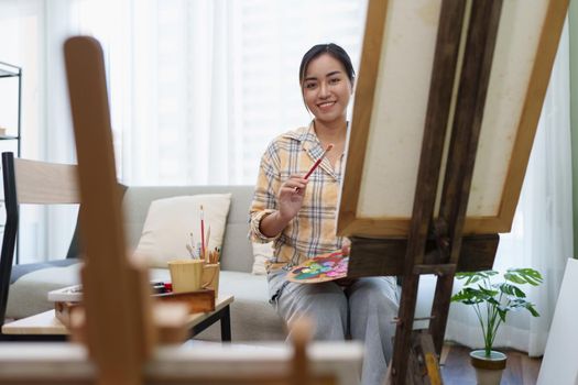 Joyful young female artist painting on canvas at workshop.