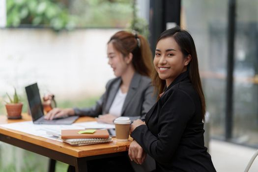 Positive Asian secretary smiling to camera during meeting at office.