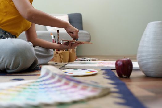 Joyful young female artist painting on canvas at workshop.