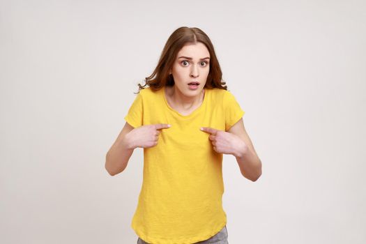 This is me. Amazed attractive teenager girl with brown hair pointing to herself with wondered expression, surprised by own success, disbelief reaction. Indoor studio shot isolated on gray background.