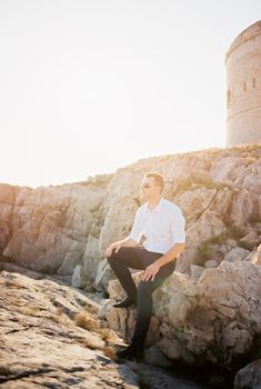 Man in sunglasses sits on a rock with a castle in the background. High quality photo