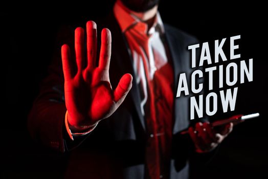 Sign displaying Take Action Now, Word for asking someone to start doing Good performance Encourage Businessman in suit holding open palm symbolizing successful teamwork.