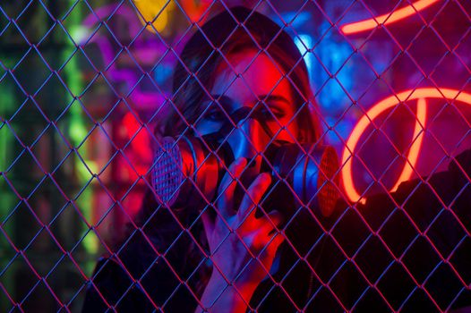 Caucasian woman in a gas mask behind a fence in a neon studio