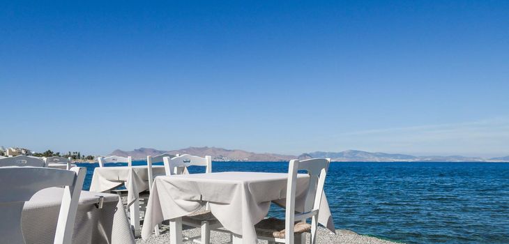 White restaurant tables on the beach in summer - travel, vacation and summer concept. The perfect lunch with a sea view