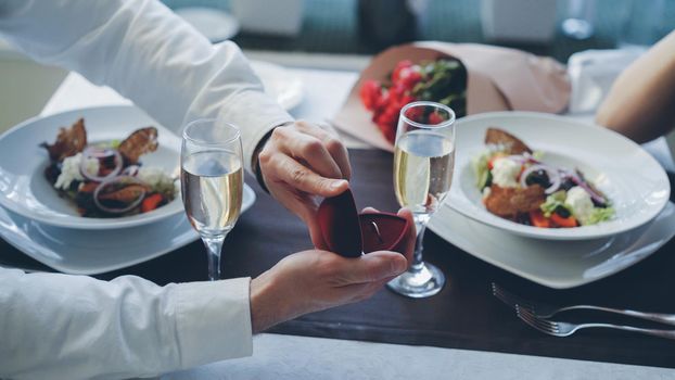 Close-up shot of beautiful ring being placed on manicured female finger during marriage proposal at romantic dinner in restaurant. Engagement and fine dining concept.