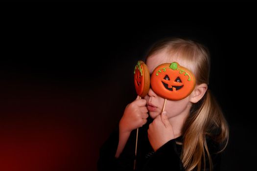 Little girl, caucasian in Halloween style. child holds a gingerbread pumpkin cookie near his eyes with a funny face. Long banner with copy space in gloomy style. The concept of homemade sweets, baking