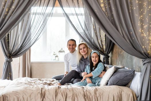 Smiling family lie on a white bed.