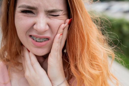 Young red-haired woman with braces suffering from pain